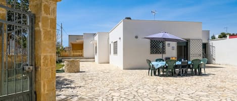 Un patio con piso de piedra, una mesa con sillas y un edificio de fachada blanca.