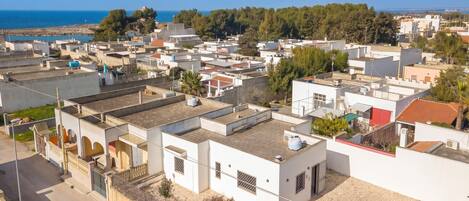 A residential area with white buildings, a paved road, and a distant view of the sea.