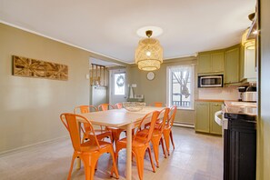 A dining area with a table and chairs, a chandelier, and kitchen cabinets. - Face au Fleuve (Grondines)