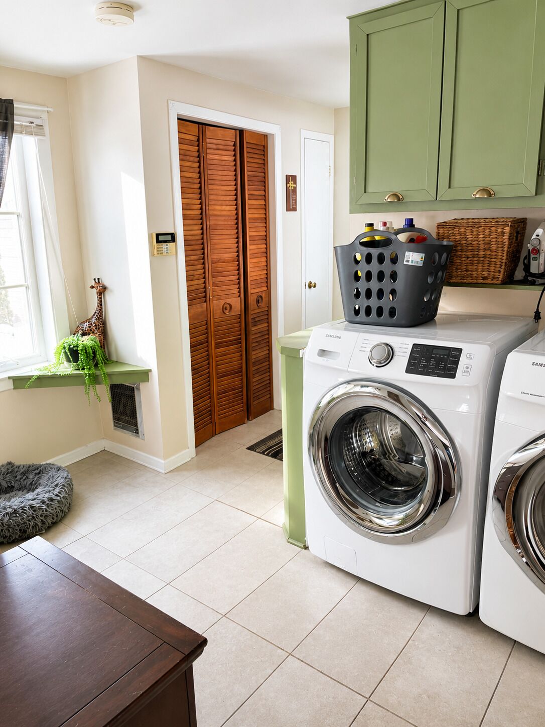 A laundry area with a front-loading washer and dryer, wooden doors, a green cabinet, and a small plant.