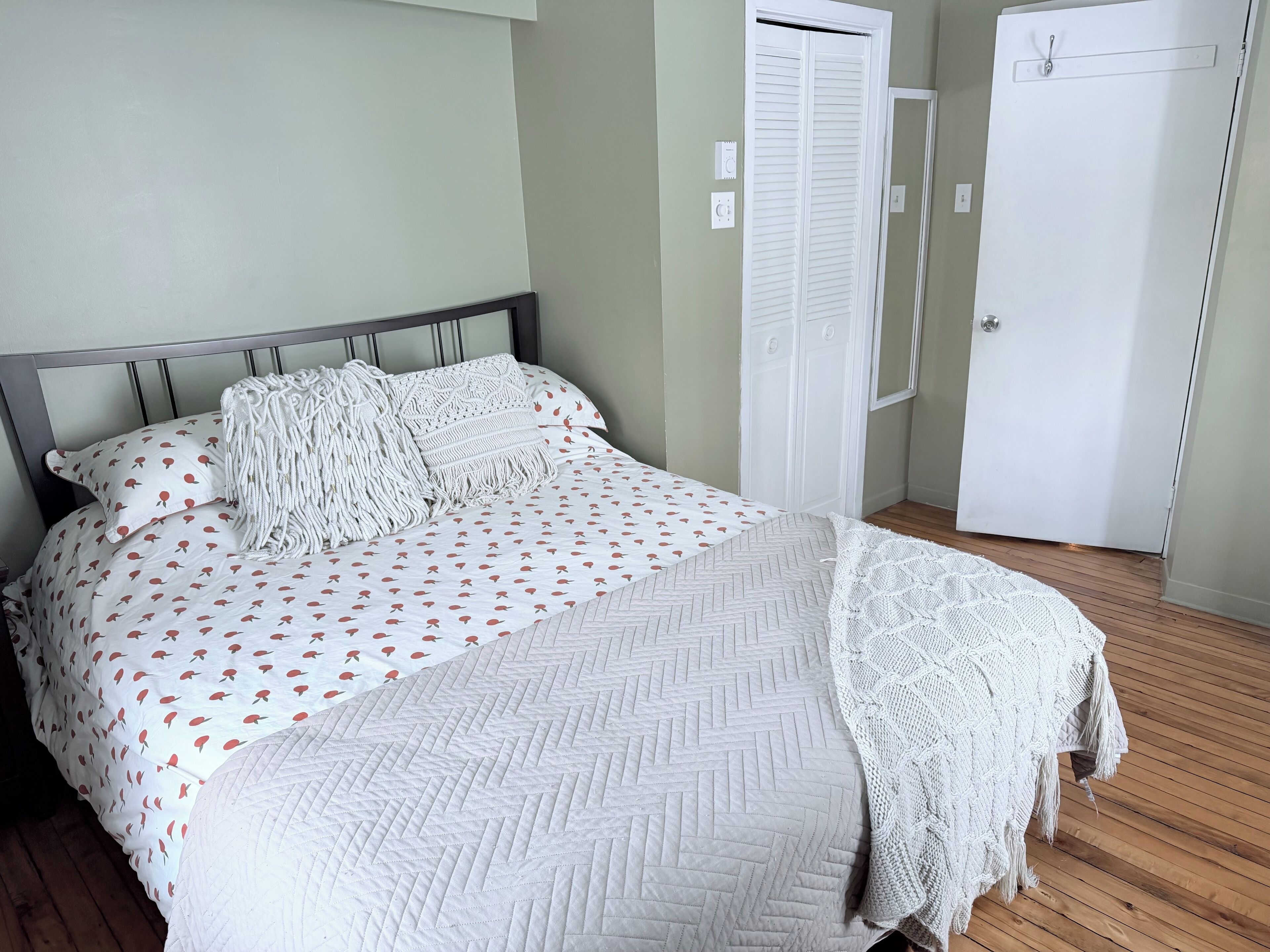 Een net opgemaakt bed met een bedspreide met een patroon, kussens, een witte gebreide plaid en een quilt met een ruitpatroon.