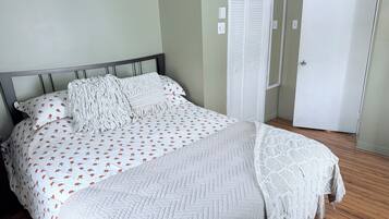 Een net opgemaakt bed met een bedspreide met een patroon, kussens, een witte gebreide plaid en een quilt met een ruitpatroon.