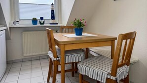A small dining area with a table and chairs, a window with a view of the sky, and a radiator below. - Steinmarner Ferienwohnung, Steinmarner Str. 25-27, 27476 Cuxhaven- Döse, Kleine Haustiere auf Anfrage (Cuxhaven- Döse)