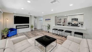 Een moderne woonkamer met een flatscreen televisie, een salontafel en een keuken met barkrukken.