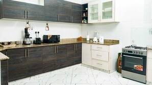 A modern kitchen with dark wood cabinets, a granite countertop, a gas stove, and a microwave. - Lux Suites Le Royal Apartments Nyali (Mombasa)