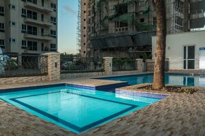 A swimming pool with a tiled edge, surrounded by a brick patio and a palm tree. - Lux Suites Le Royal Apartments Nyali (Mombasa)