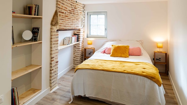 Une chambre à coucher avec un lit, des tables de chevet, une fenêtre et un mur décoré d’un motif en briques.