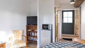 Un espace de vie compact comprenant une chaise en bois, une bibliothèque, un petit réfrigérateur et un téléviseur.