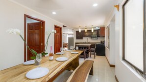A dining area with a wooden table, white plates, and wine glasses. There are two doors leading to other rooms, and a kitchen area with dark cabinets and a microwave.