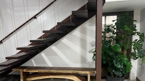 A modern staircase with wooden steps and metal railings, a wooden bench at the bottom, and a large potted plant beside it.