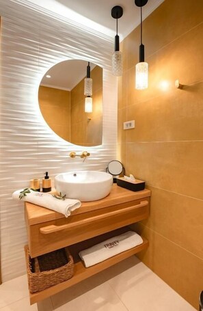 A modern bathroom with a round mirror, a white sink, and wooden vanity.