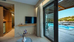 A modern living room with a TV, a vase with flowers, and a view of a swimming pool and outdoor seating. - Trinity Design Suites (Parga)
