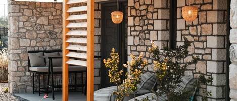 A stone exterior with a wooden pergola, outdoor seating, and hanging lights.