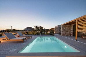 A rectangular swimming pool with lounge chairs and a stone wall on one side.