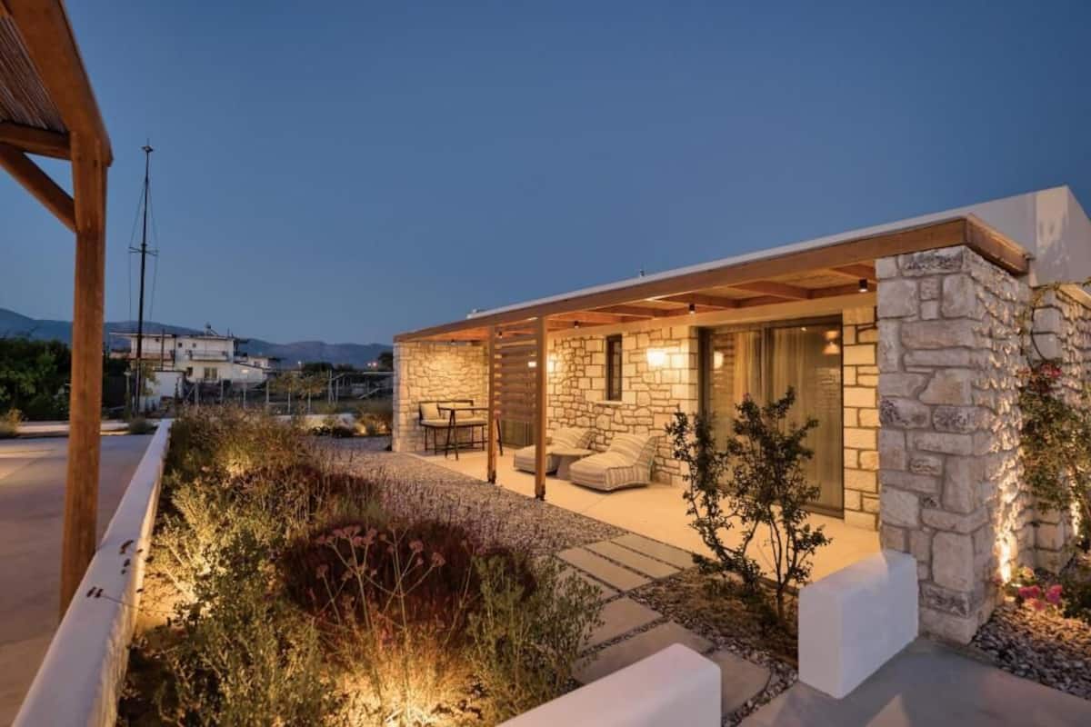 A modern house with a stone exterior, a covered patio with outdoor furniture, and a view of the surrounding landscape.