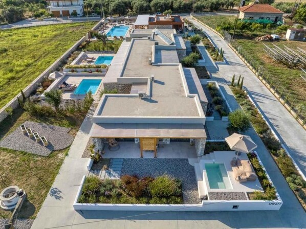 A modern villa with multiple swimming pools, a covered patio, and a landscaped garden.