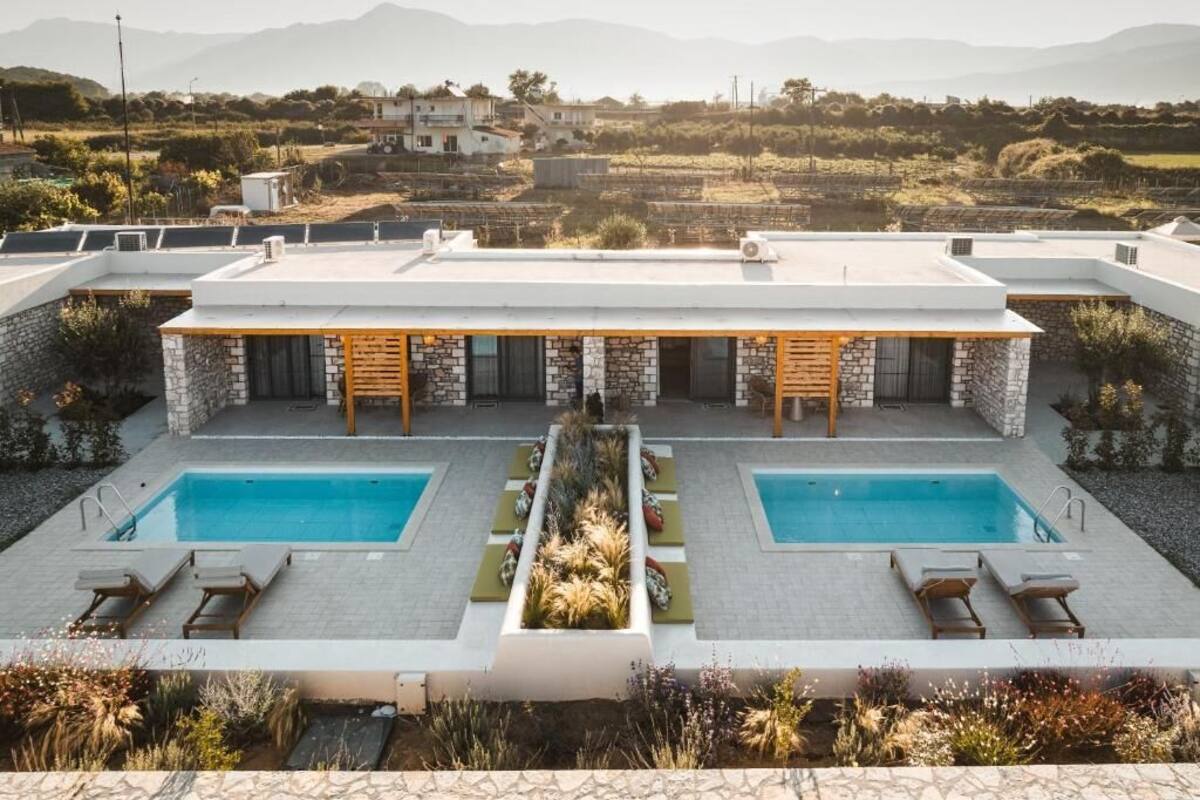 A modern villa with two swimming pools, a stone facade, and a view of the countryside.