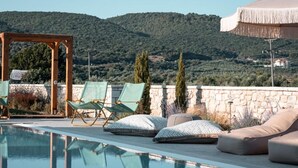 A poolside area with lounge chairs and a pergola, set against a mountainous backdrop. - Trinity Design Suites (Parga)