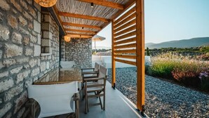 A covered outdoor seating area with stone walls, wooden beams, and a view of the landscape. - Trinity Design Suites (Parga)