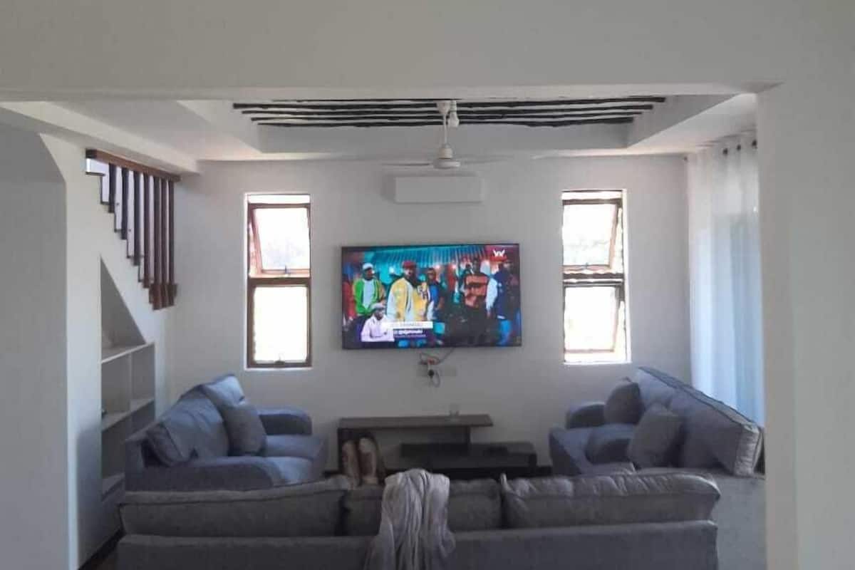 Een moderne woonkamer met een grote grijze modulaire bank, een flatscreen televisie aan de muur en een trap aan de linkerkant.