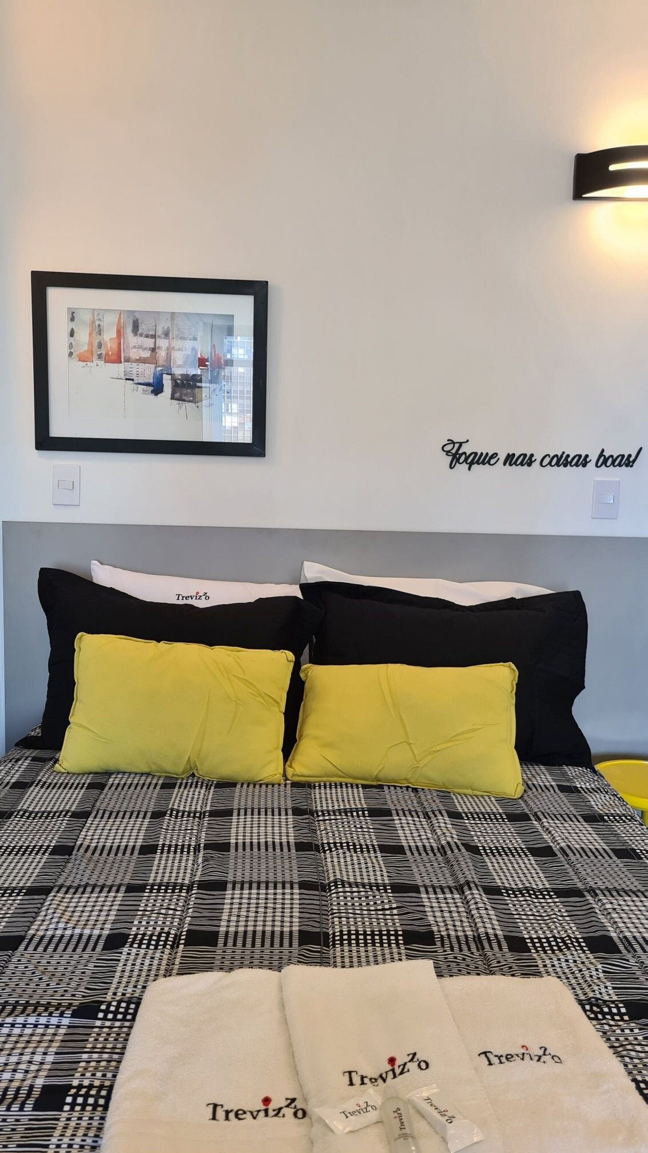 Camera da letto con un letto caratterizzato da biancheria a quadri bianco e nero, due cuscini gialli e un quadro incorniciato sopra il letto.