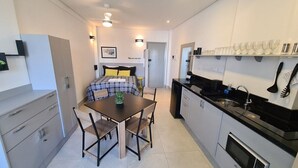 Una habitación de hotel compacta con cama, una pequeña mesa de comedor, kitchenette y baño.