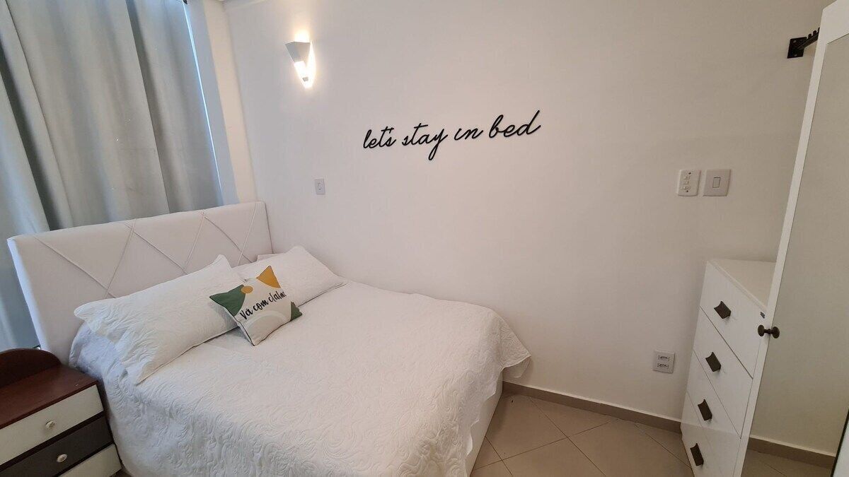 Un letto ben rifatto con un cuscino decorativo, una lampada a parete e una frase motivazionale.