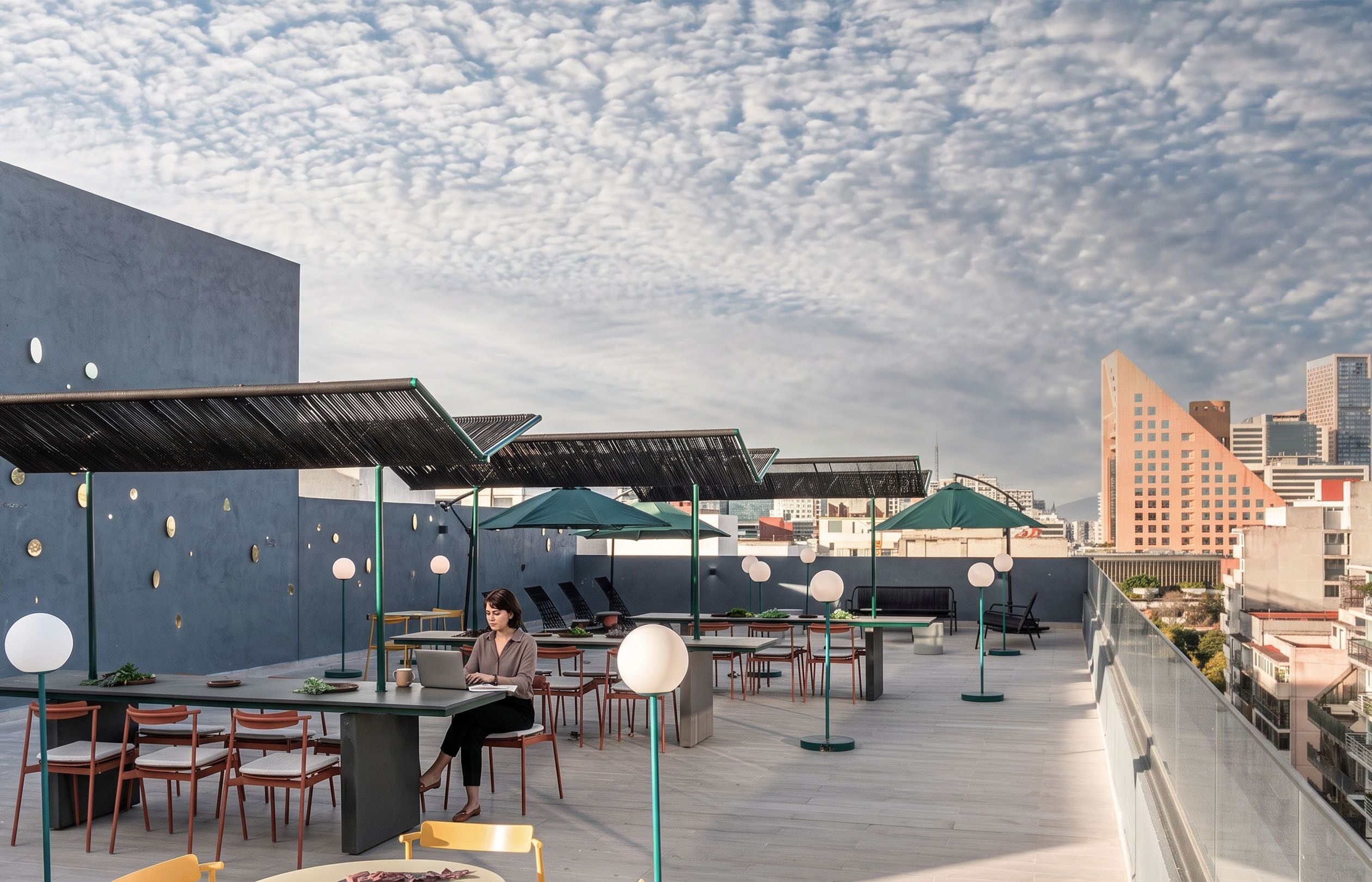 An outdoor dining area with tables and chairs, umbrellas, and a cityscape in the background.