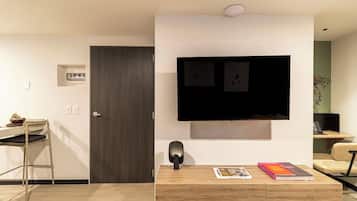 Una sala de estar moderna con una puerta de madera oscura, un televisor de pantalla plana montado en la pared, una mesa de centro de madera con libros y un escritorio con una silla.