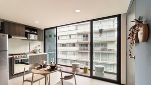 Ett modernt kök med en matplats, ett stort fönster med utsikt över en byggnad och en växt på väggen.