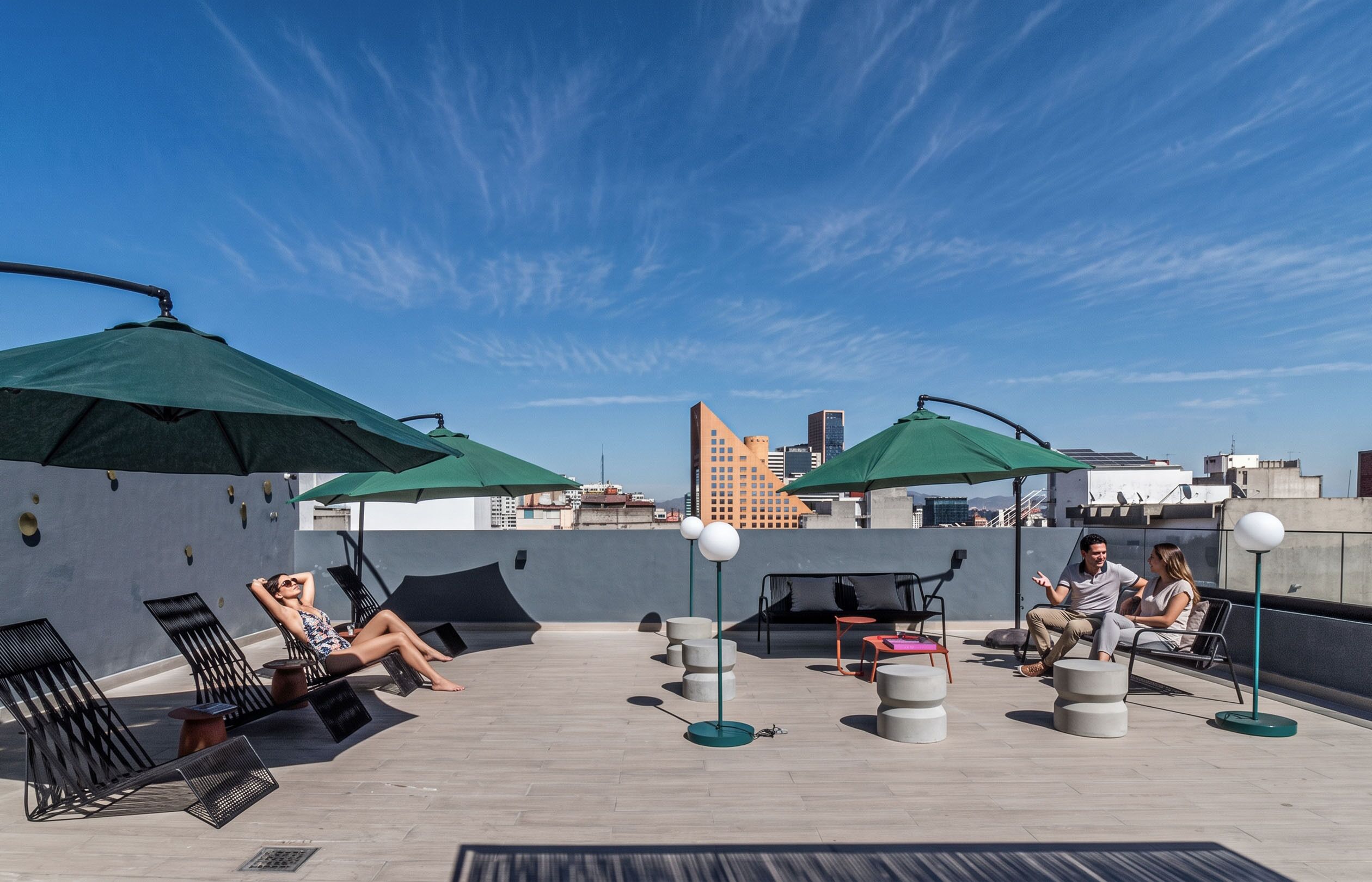 Terraza en la azotea con mobiliario exterior, sombrillas y vistas a la ciudad.