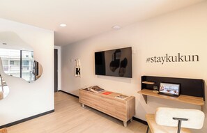A modern hotel room with a wooden floor, a desk with a laptop, a chair, a TV on the wall, and a #staykukun sign. - Kukun Sócrates Polanco (Mexico City)