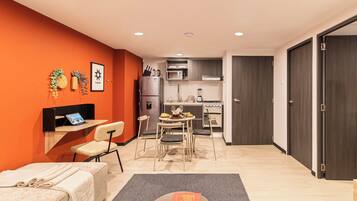Un espacio habitable compacto con kitchenette, comedor y una pequeña zona de estar con sofá y mesa.