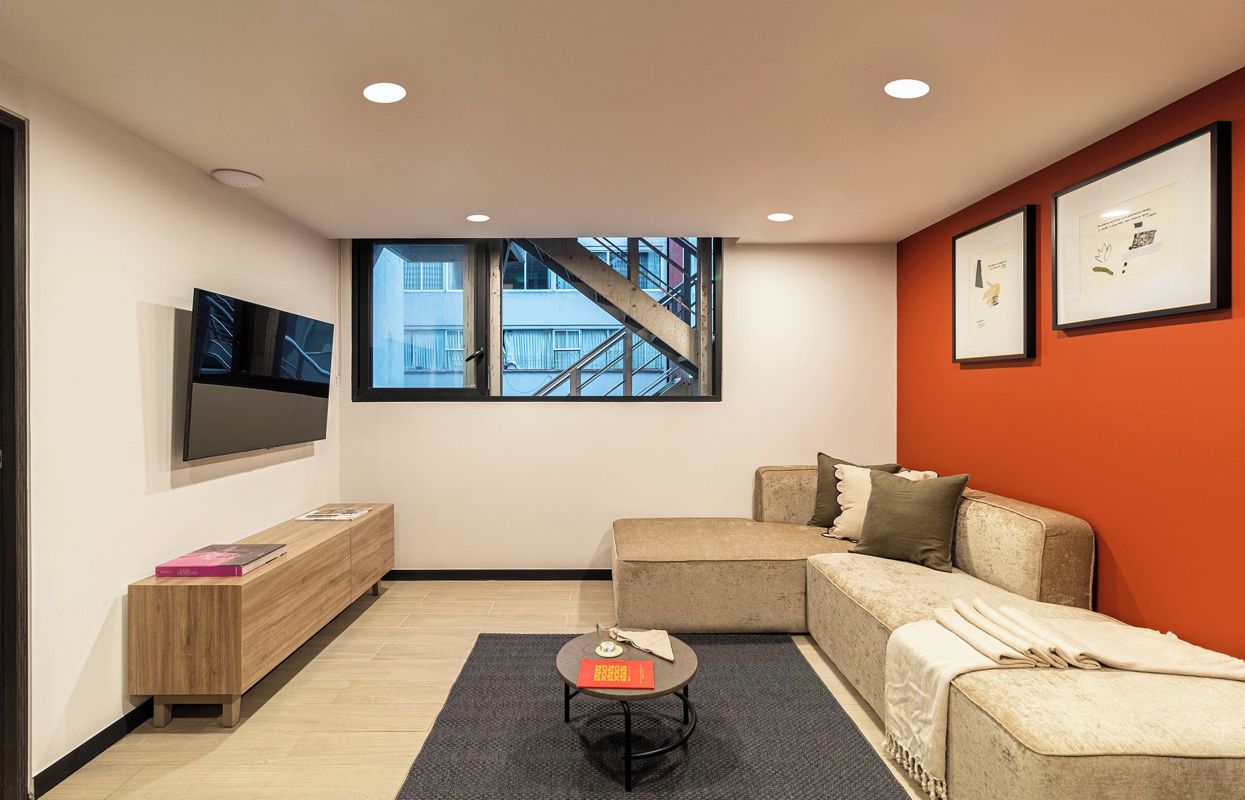 Una sala moderna con un sofá, una mesa de centro, un televisor y un ventanal con vista a un edificio.