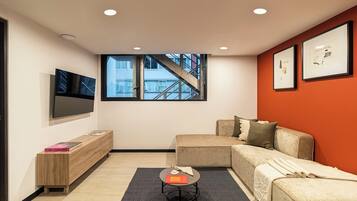 Una sala moderna con un sofá, una mesa de centro, un televisor y un ventanal con vista a un edificio.