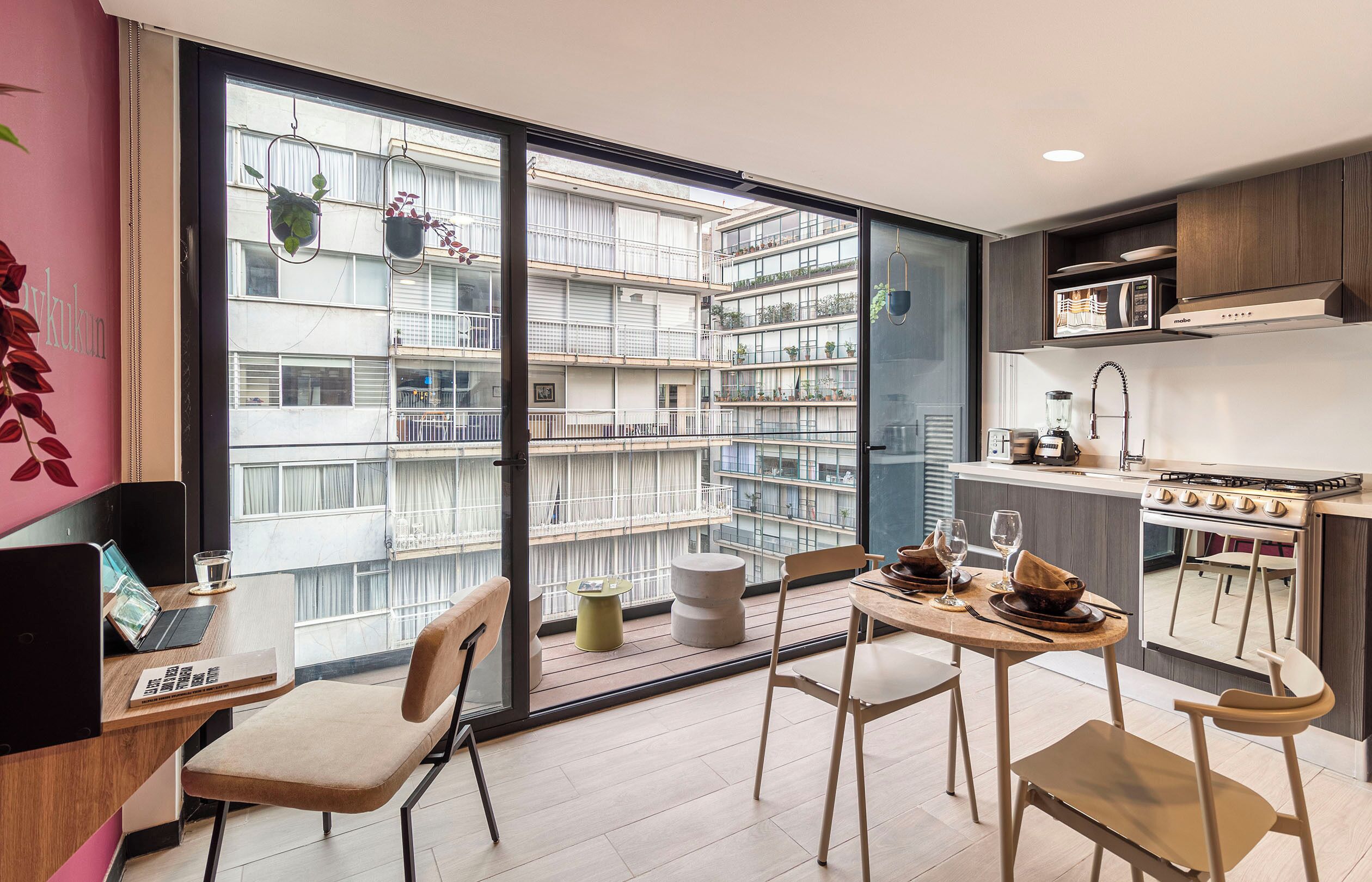 Una cocina moderna con comedor, estufa empotrada y vista a un edificio residencial con balcones.