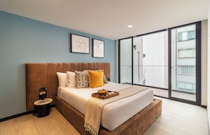 A bedroom with a large bed, a bedside table, a lamp, and a window with a view of buildings. - Kukun Sócrates Polanco (Mexico City)