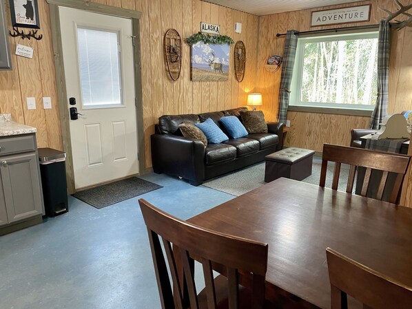 L’intérieur chaleureux d’un chalet, avec un décor en bois, un canapé en cuir, une table à manger avec des chaises et une fenêtre donnant sur la forêt.