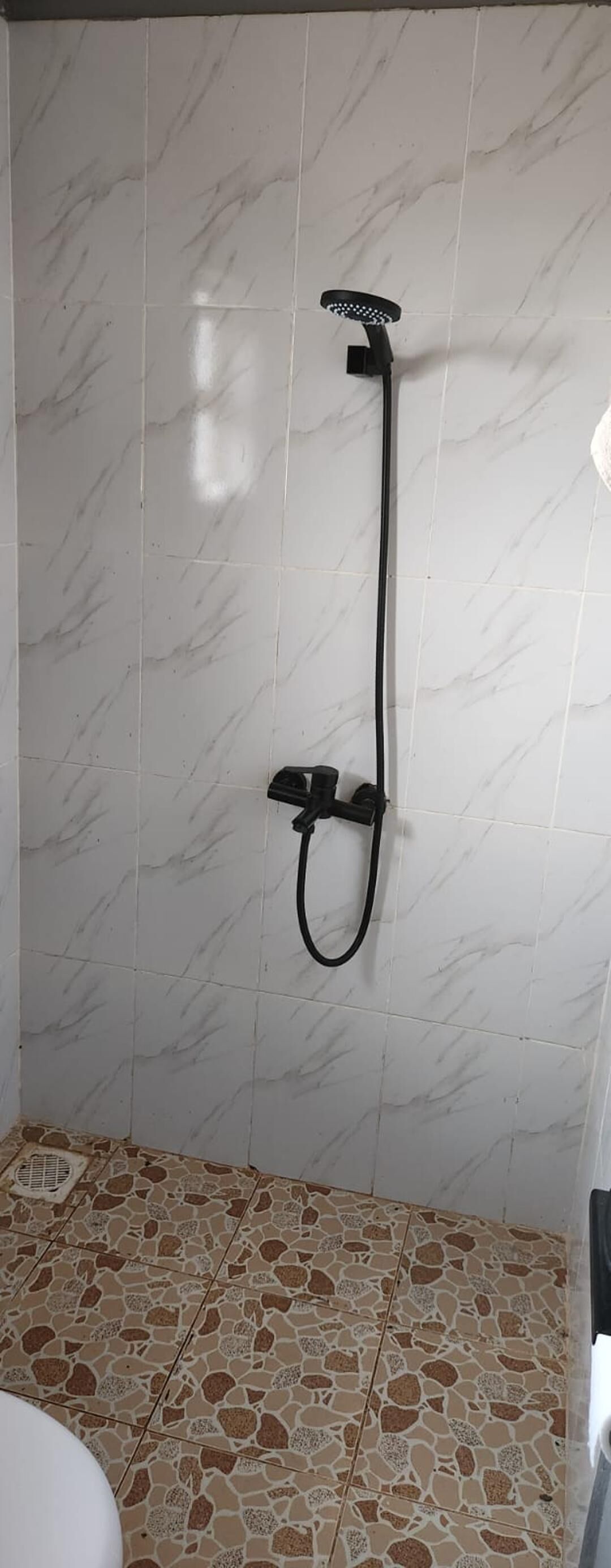 Un baño con ducha, azulejos de mármol blanco y suelo de baldosas con motas.