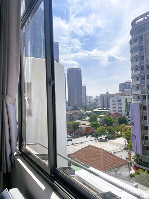 A view from a window overlooking a cityscape with tall buildings, a clear sky, and a street below.