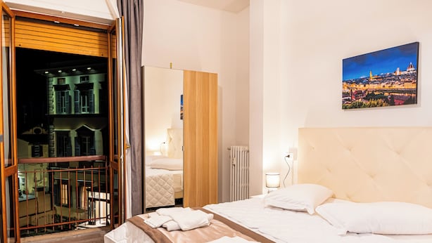 Une chambre d’hôtel avec un lit, un grand miroir, une vue sur la ville et une porte en bois donnant sur un espace extérieur.