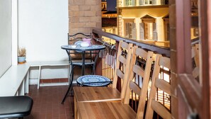 Un balcon doté de mobilier en bois et d’une table, offrant une vue sur un immeuble avec de nombreuses fenêtres et des balcons.