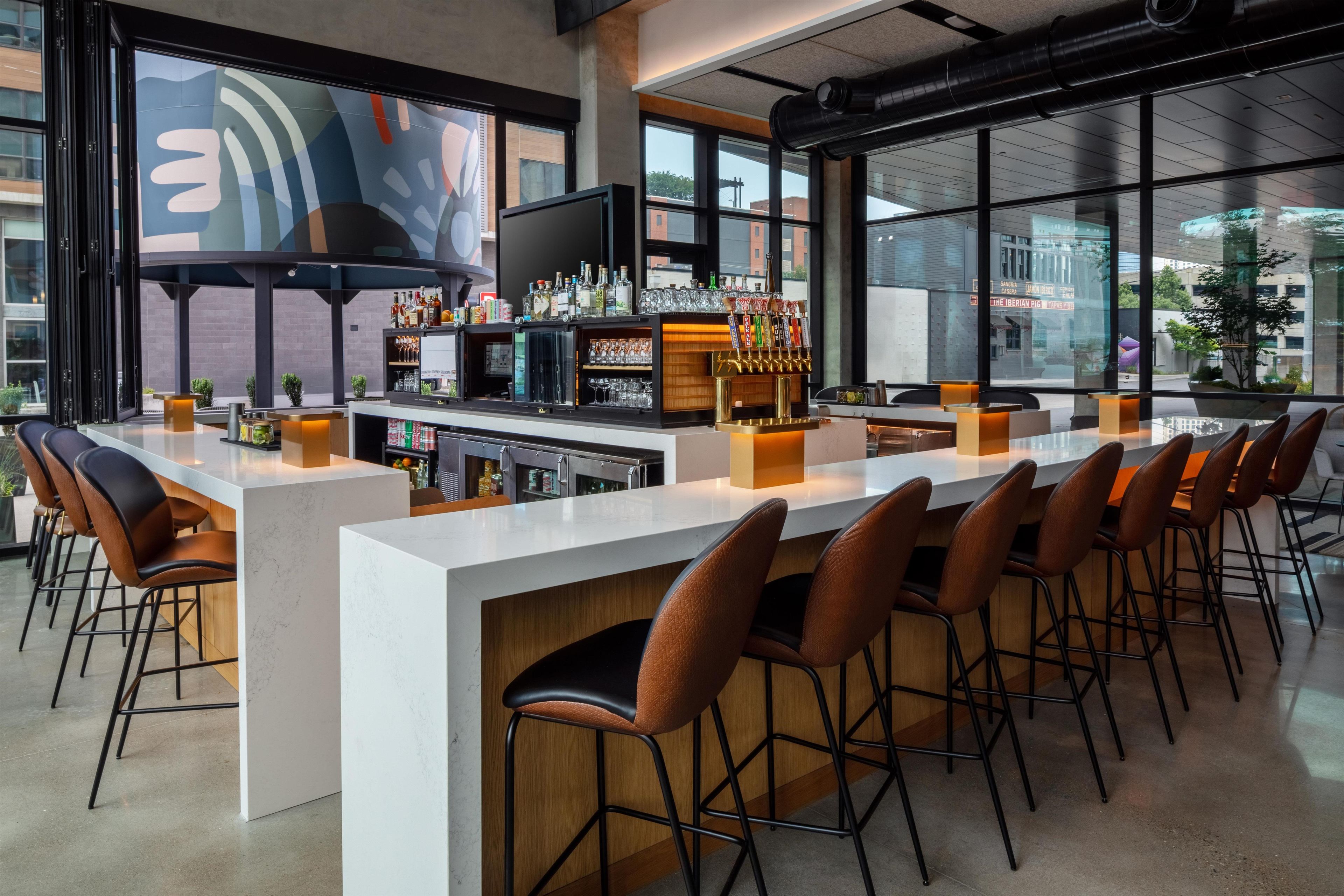 Una zona de bar con una barra larga, varios taburetes y una amplia variedad de botellas y vasos.