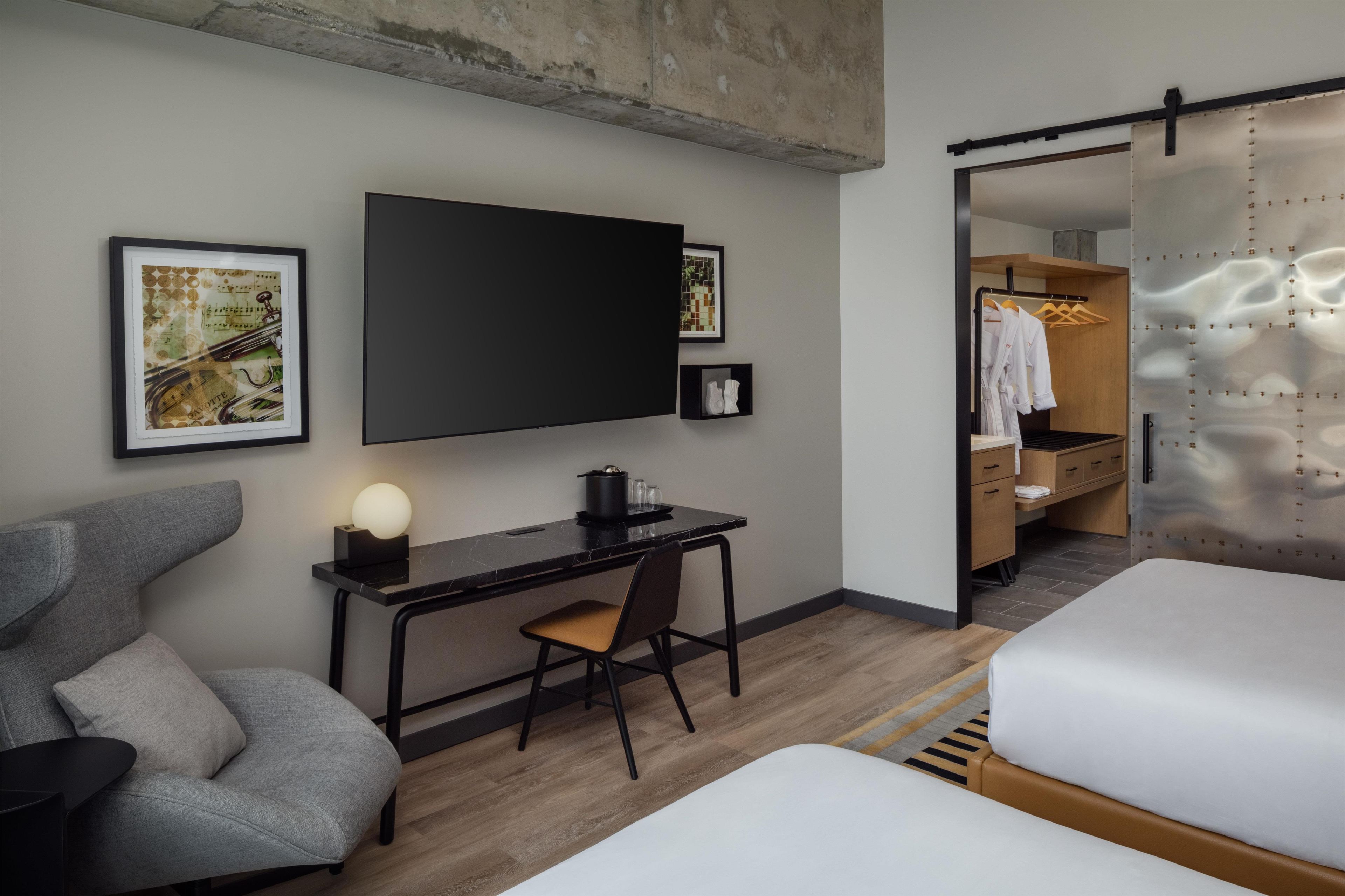 Ein modernes Hotelzimmer mit Schreibtisch, Stuhl, Bett und begehbarem Kleiderschrank.