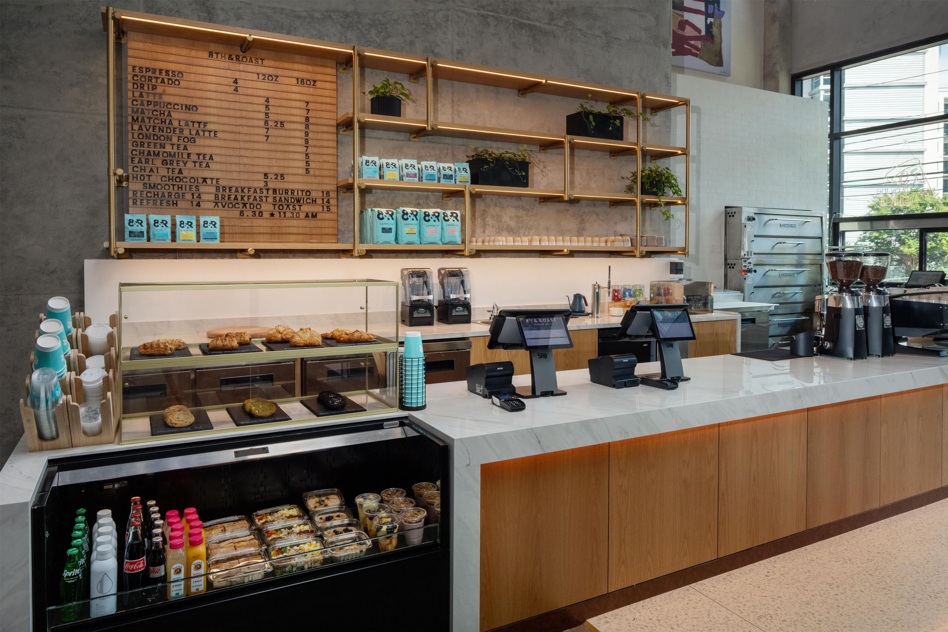 Mostrador de cafetería con menú, granos de café y una variedad de pasteles y sándwiches.
