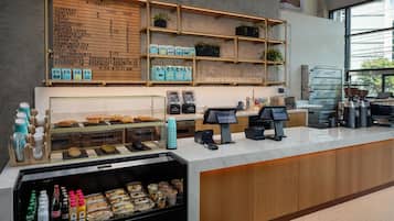 Mostrador de cafetería con menú, granos de café y una variedad de pasteles y sándwiches.