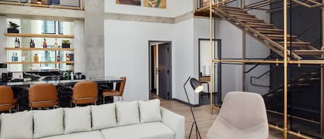A modern interior with a sofa, dining area, staircase, and artwork.