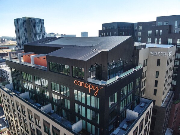 Ein modernes Hotelgebäude mit einer auffälligen „Canopy“-Beschilderung, das eine Dachterrasse und mehrere Geschosse mit großen Fenstern bietet.