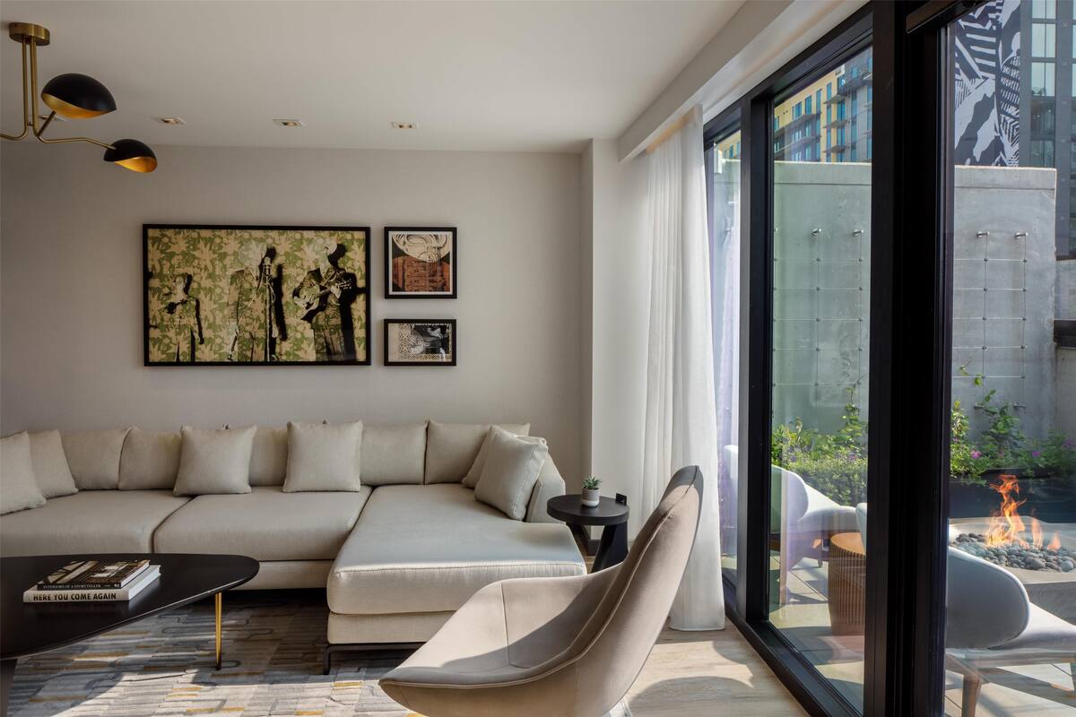 A modern living room with a sectional sofa, a coffee table, and a glass wall offering a view of a courtyard with a fire pit.