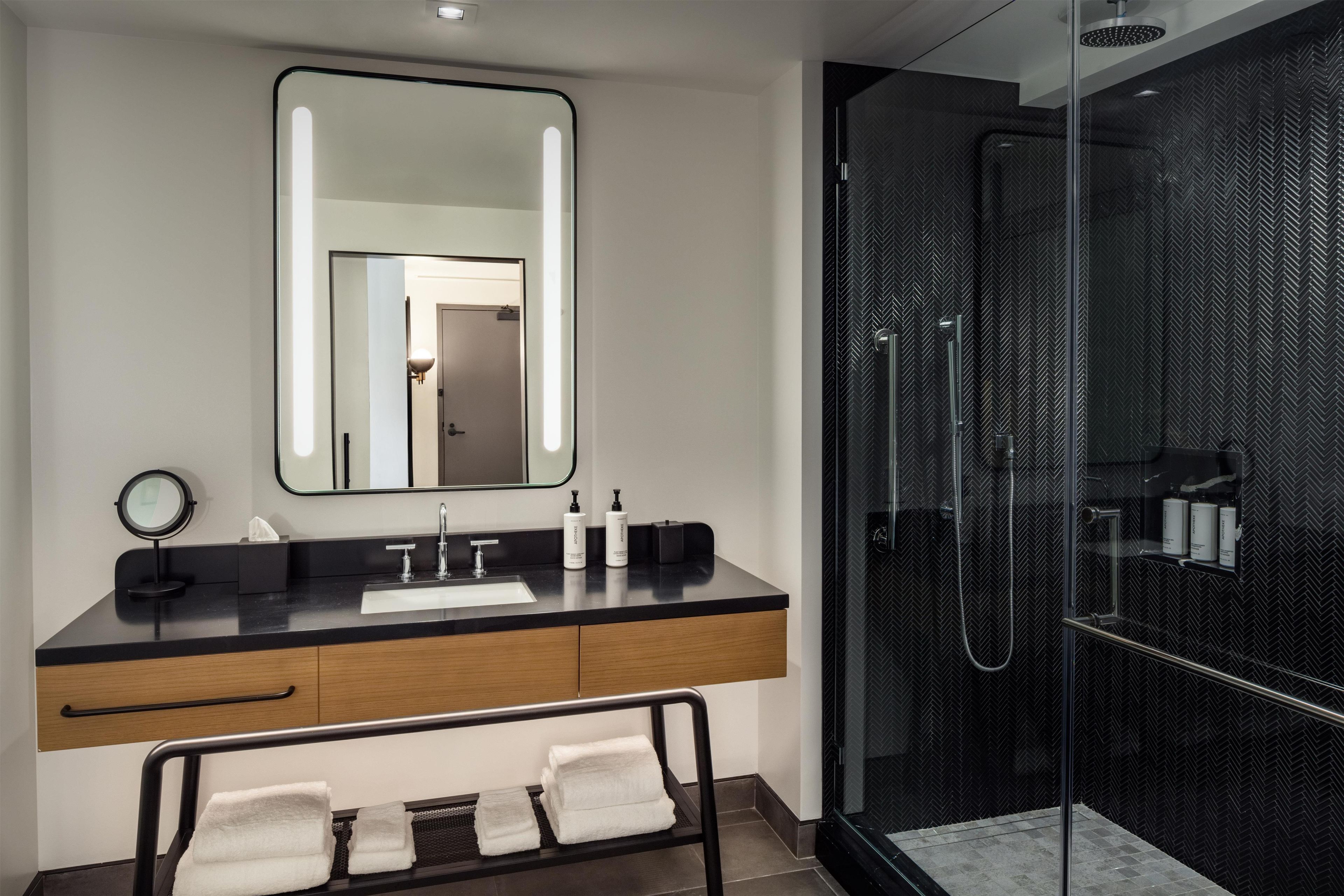 A modern bathroom with a large mirror, a sink, and a glass-enclosed shower.